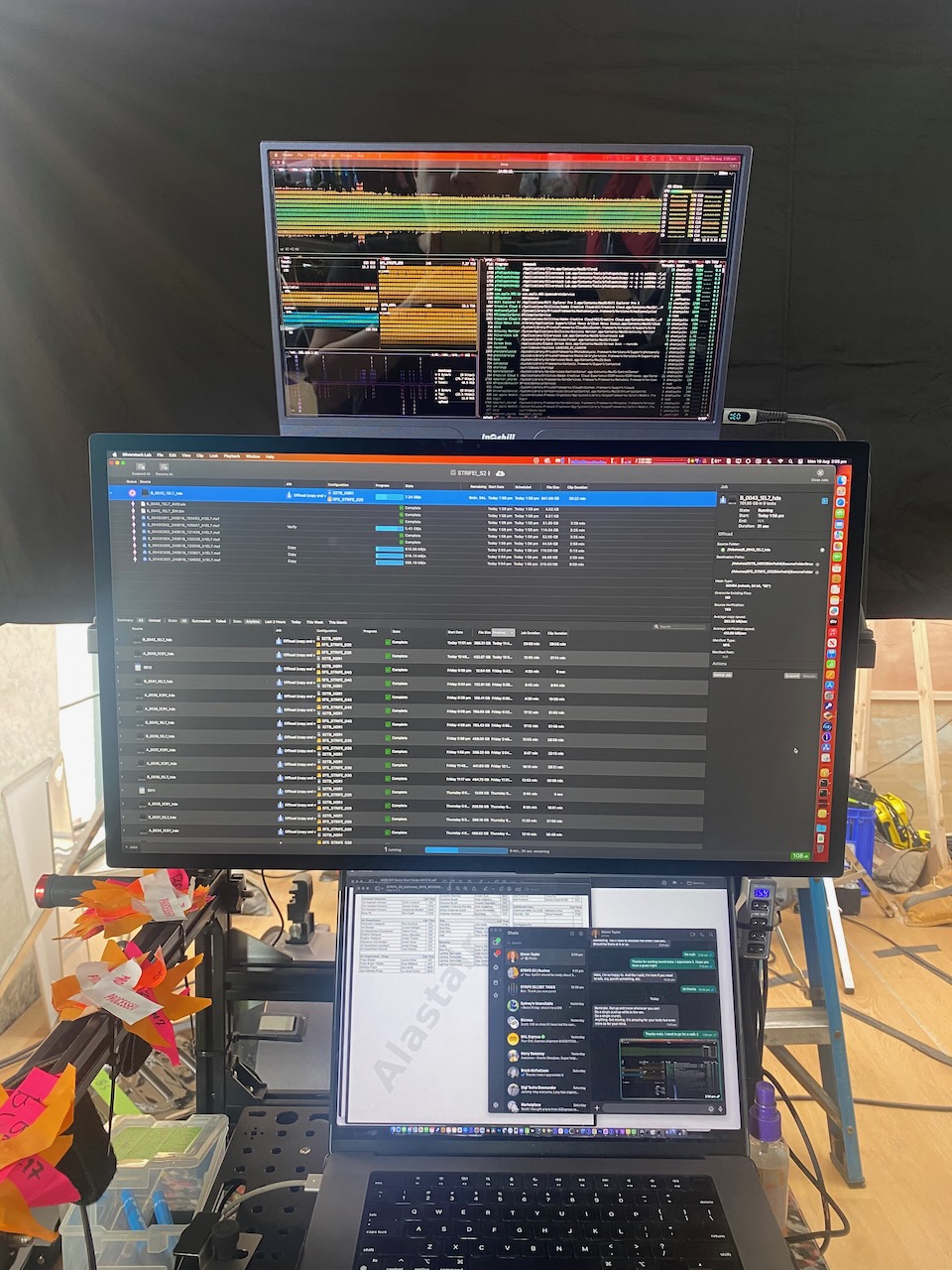 Workspace featuring two computer monitors displaying data and a laptop with messaging app, set up in an indoor environment.