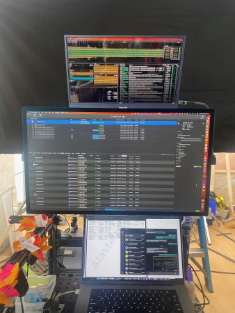 Workspace featuring two computer monitors displaying data and a laptop with messaging app, set up in an indoor environment.