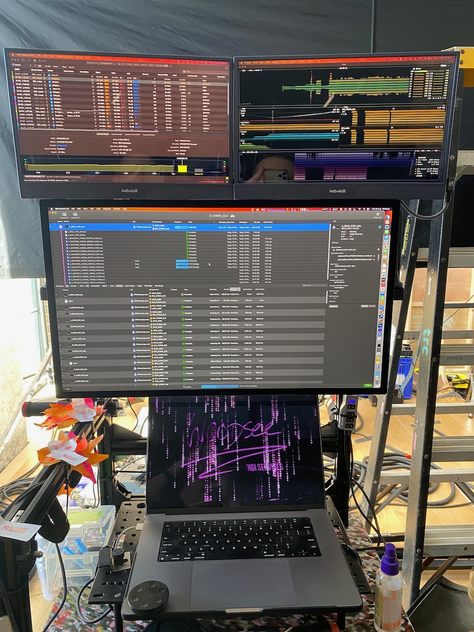 Workspace with a laptop, monitors displaying data, and a ladder in the background. Technology and home office setup with computer screens.