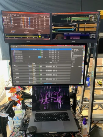 Workspace with a laptop, monitors displaying data, and a ladder in the background. Technology and home office setup with computer screens.