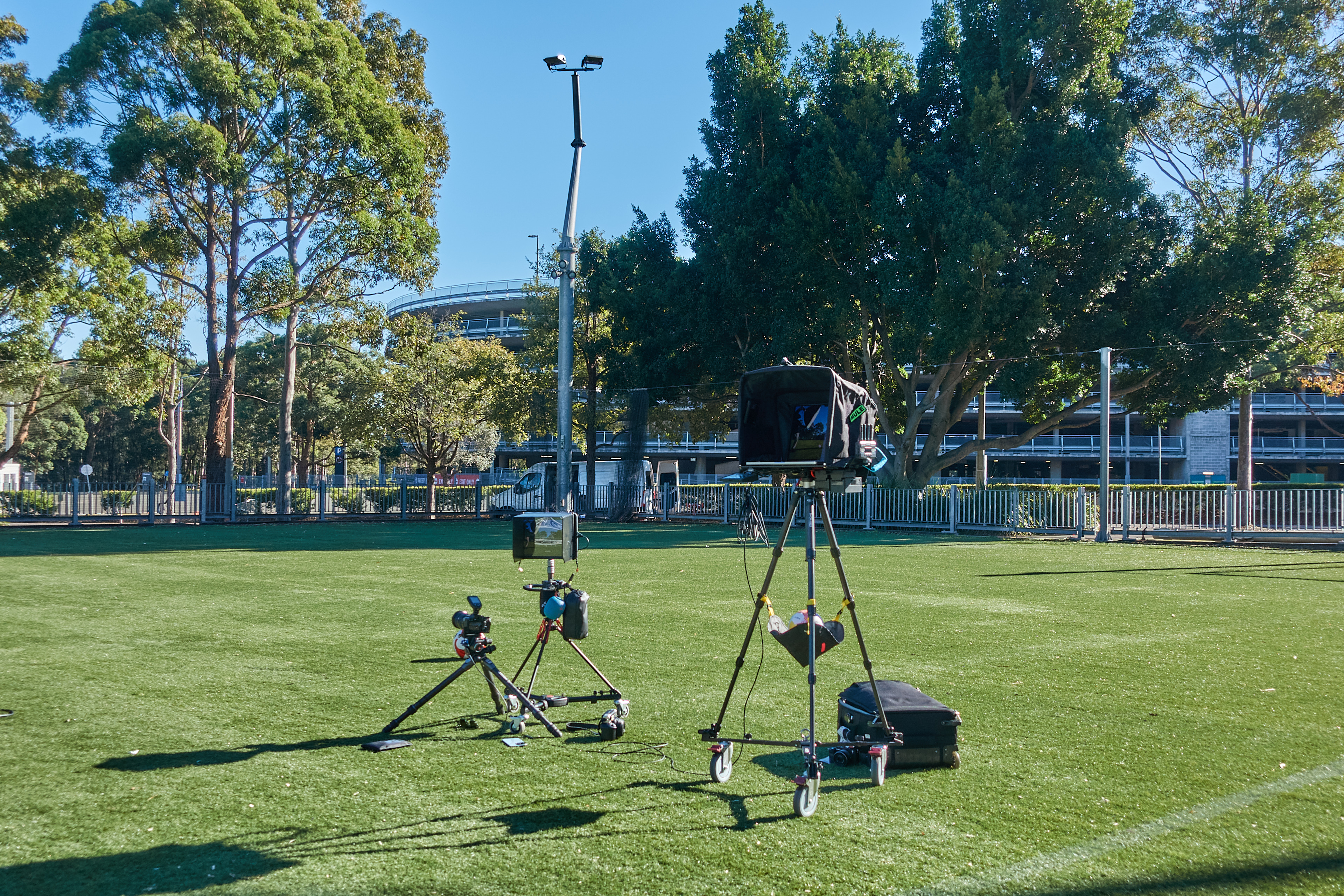 Outdoor scene featuring two camera setups, one equipped with a telephoto lens and the other with a video camera rig on a sunny day.