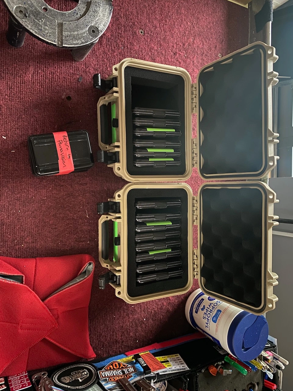 Overhead view of two open tan equipment cases filled with media drives on red carpet next to a small black case with red tape.