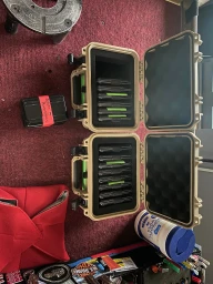 Overhead view of two open tan equipment cases filled with media drives on red carpet next to a small black case with red tape.