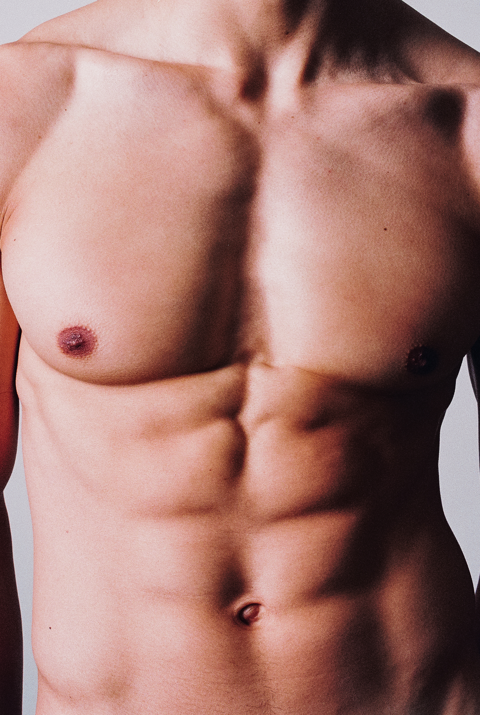Close-up studio shot of a shirtless adult male torso with defined abdominal muscles and fair skin, illuminated by soft, diffused lighting.