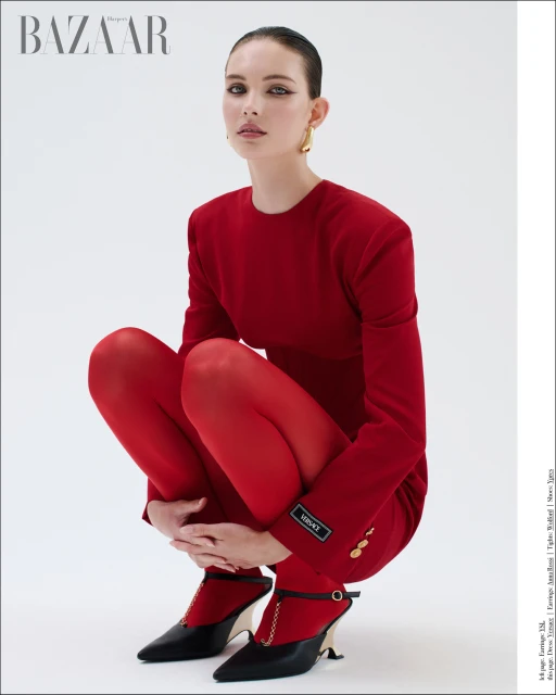A young woman in a red blazer, red tights, and black high heels poses against a white backdrop in a fashion editorial shot.
