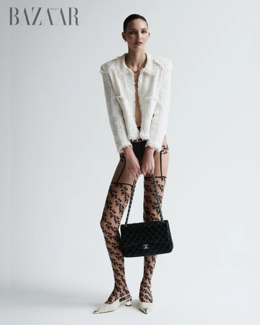 Fashion editorial shot of a woman in a bouclé jacket, black lingerie, patterned tights, slingbacks and a quilted leather bag.