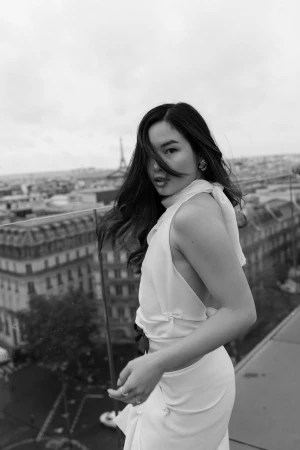 Monochrome portrait of a woman in a white halter top on a city rooftop overlooking urban buildings.