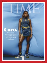 Coco Gauff standing against a bright blue fabric backdrop wearing a navy athletic top and matching skirt with yellow trim