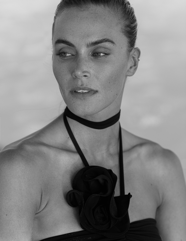 Monochrome portrait of a woman with light skin wearing a black choker and a black fabric flower on her top.