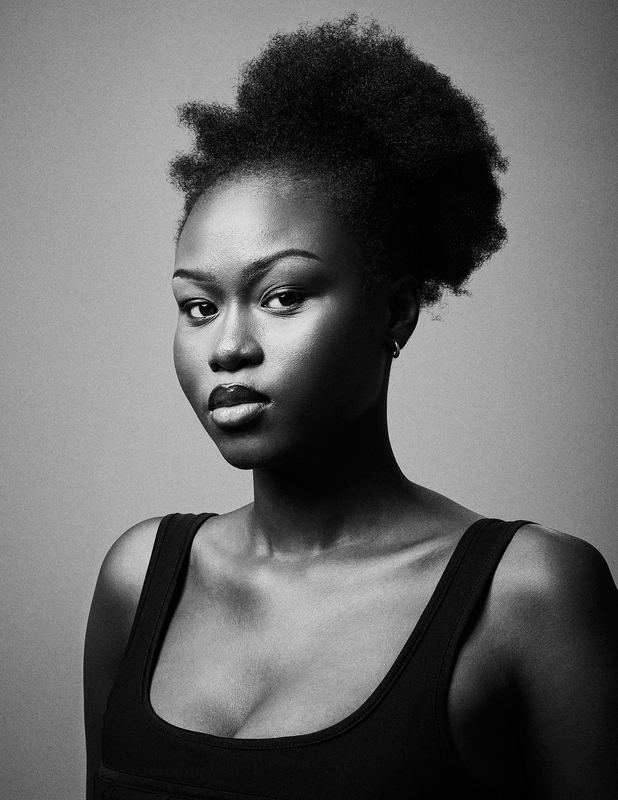 Black and white portrait of an African American woman with an afro wearing a tank top against a gray background in a photo studio.