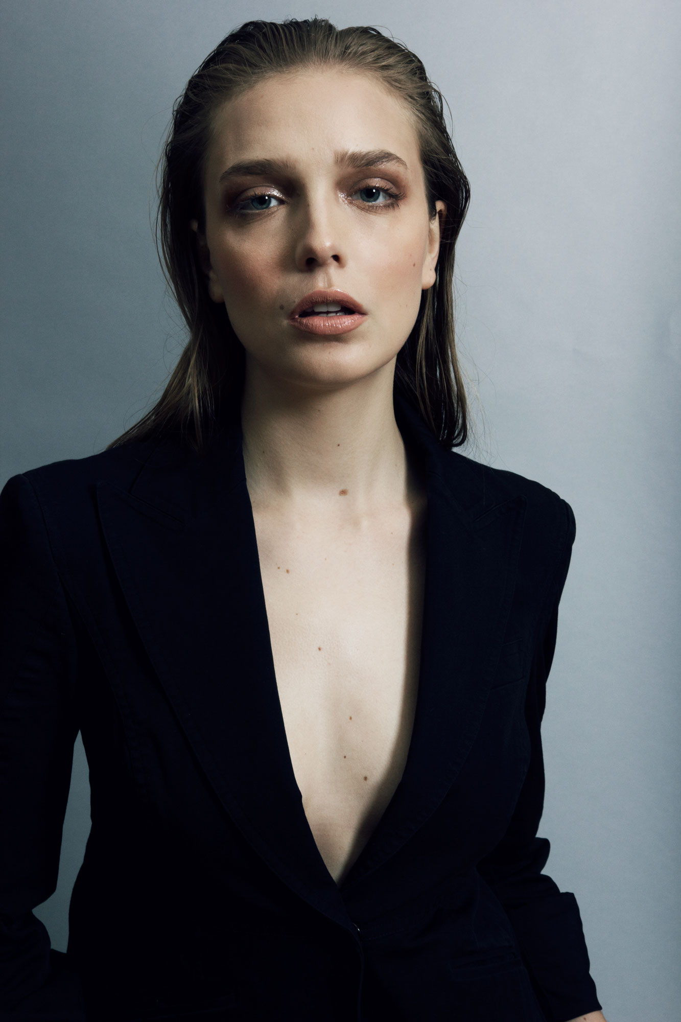 Portrait of a woman with wet hair wearing a black blazer against a grey backdrop