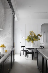 Modern kitchen interior with black cabinetry, white marble countertops, a round dining table with black chairs, and a large yellow floral arrangement.