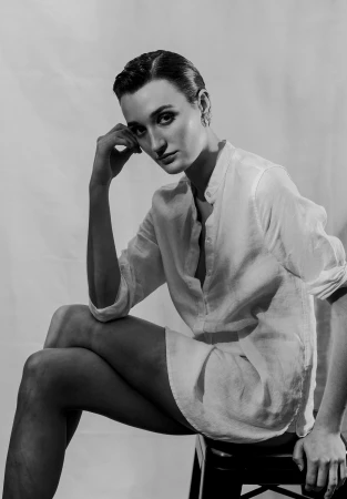 Black and white portrait of a woman seated on a stool wearing a button-down shirt against a seamless background