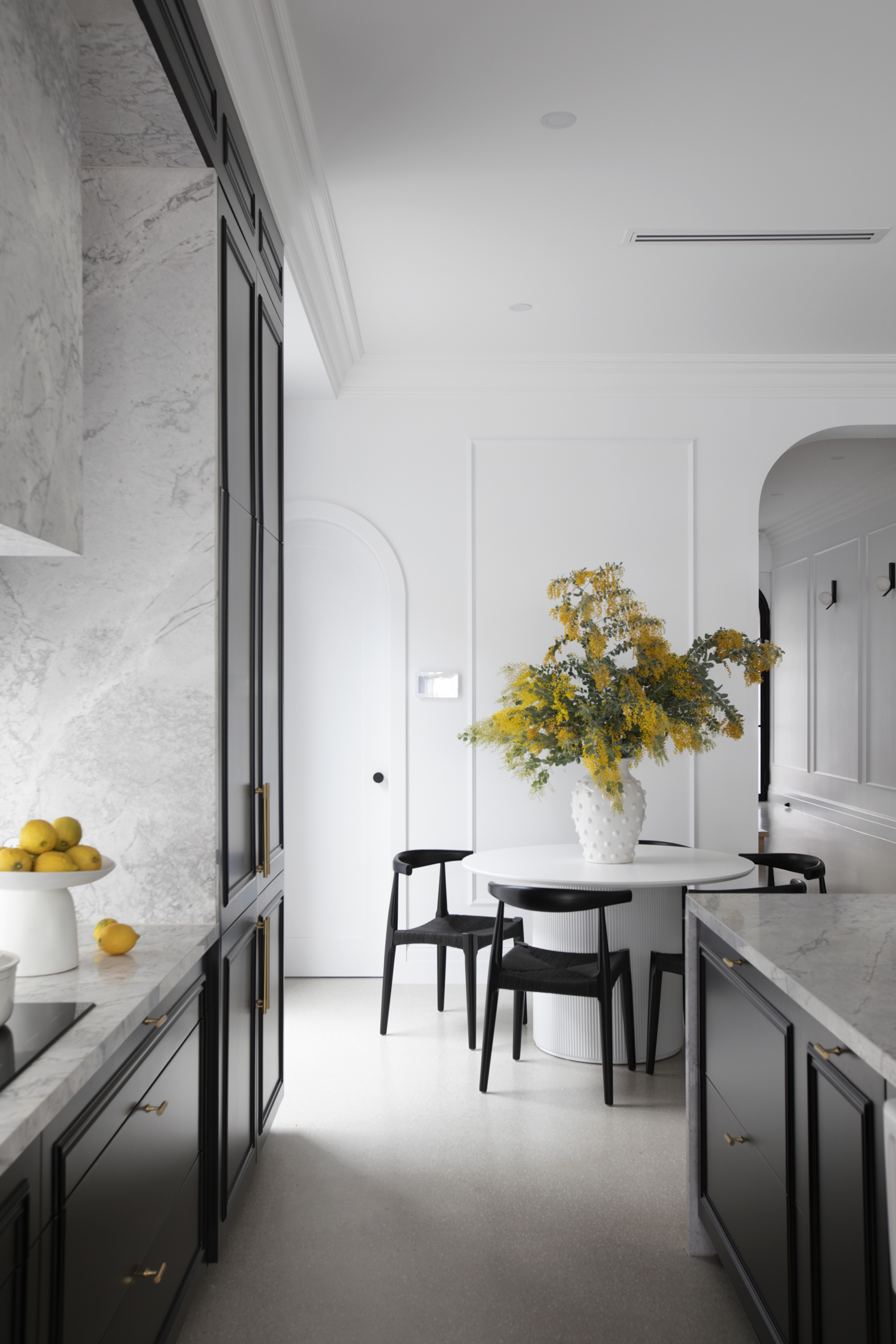 Contemporary kitchen interior featuring black cabinets, marble countertops, a round dining table with a floral arrangement, and minimalist decor.