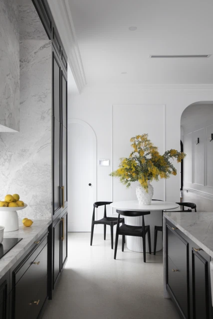 Contemporary kitchen interior featuring black cabinets, marble countertops, a round dining table with a floral arrangement, and minimalist decor.