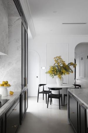 Contemporary kitchen interior featuring black cabinets, marble countertops, a round dining table with a floral arrangement, and minimalist decor.