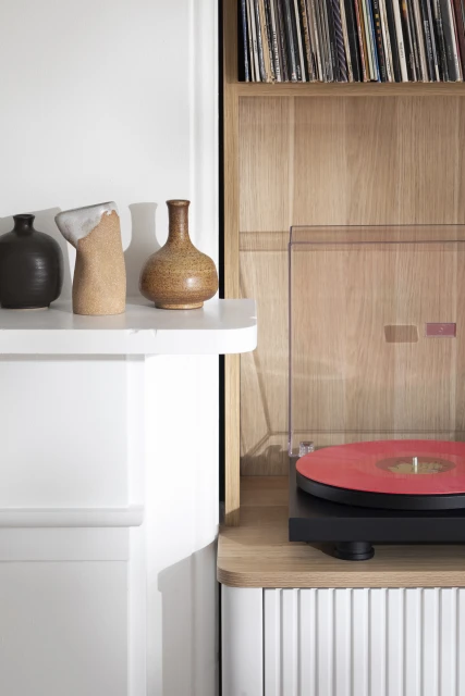 Interior shot featuring a turntable with a red record, set within a light wood cabinet, complemented by decorative vases on a white shelf.