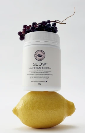 Beauty product container sits atop a lemon with dark grapes, on a white backdrop showcasing a vibrant and healthy aesthetic.