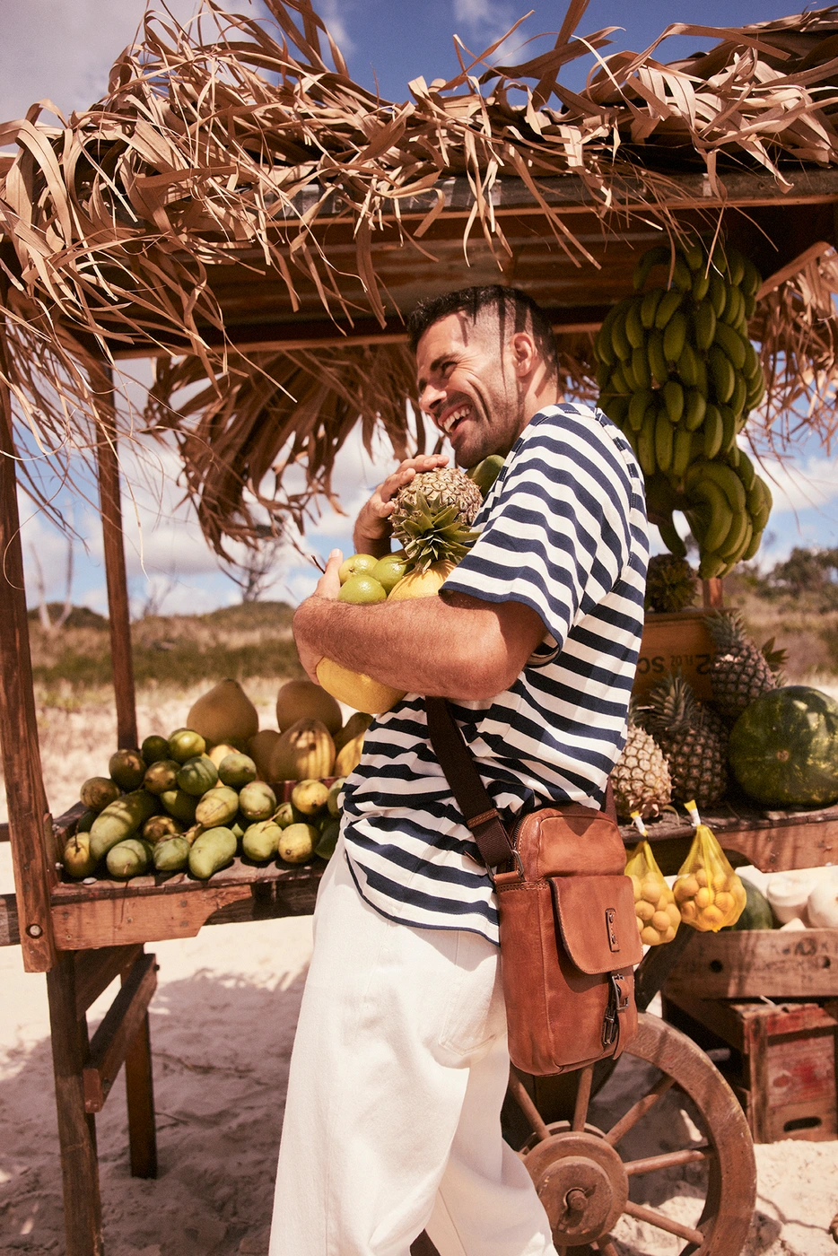 A smiling man holding pineapples in front of a fruit stall styled by Caitlin Melling