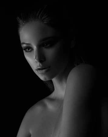 Close-up monochrome portrait of a woman with wet-look hair lit dramatically against a black background