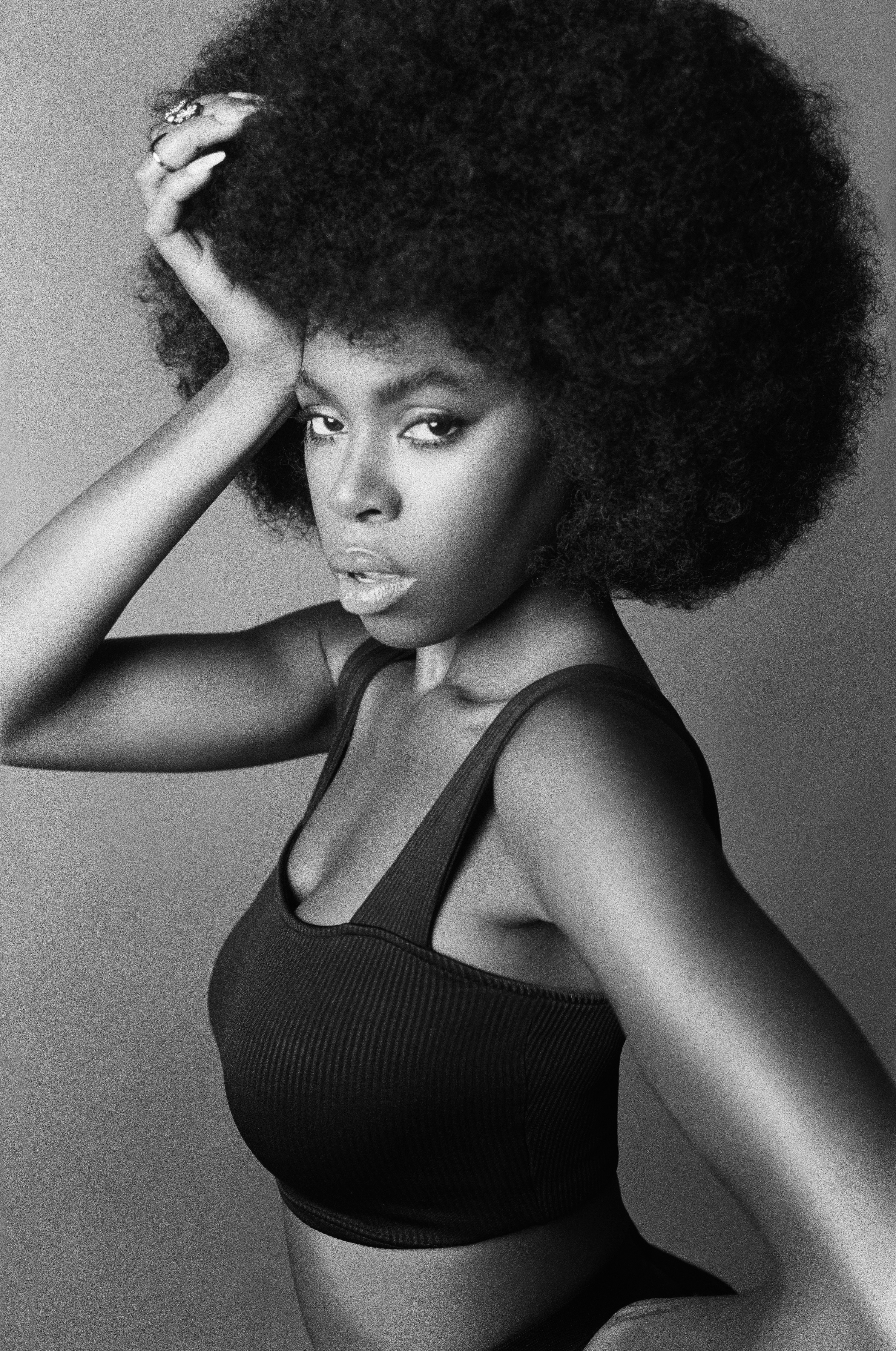 Black and white portrait of an African American woman with a large afro wearing a ribbed crop top in a studio setting.