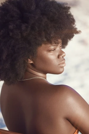 Close-up portrait of a Black woman with voluminous afro hair looking over her shoulder outdoors.
