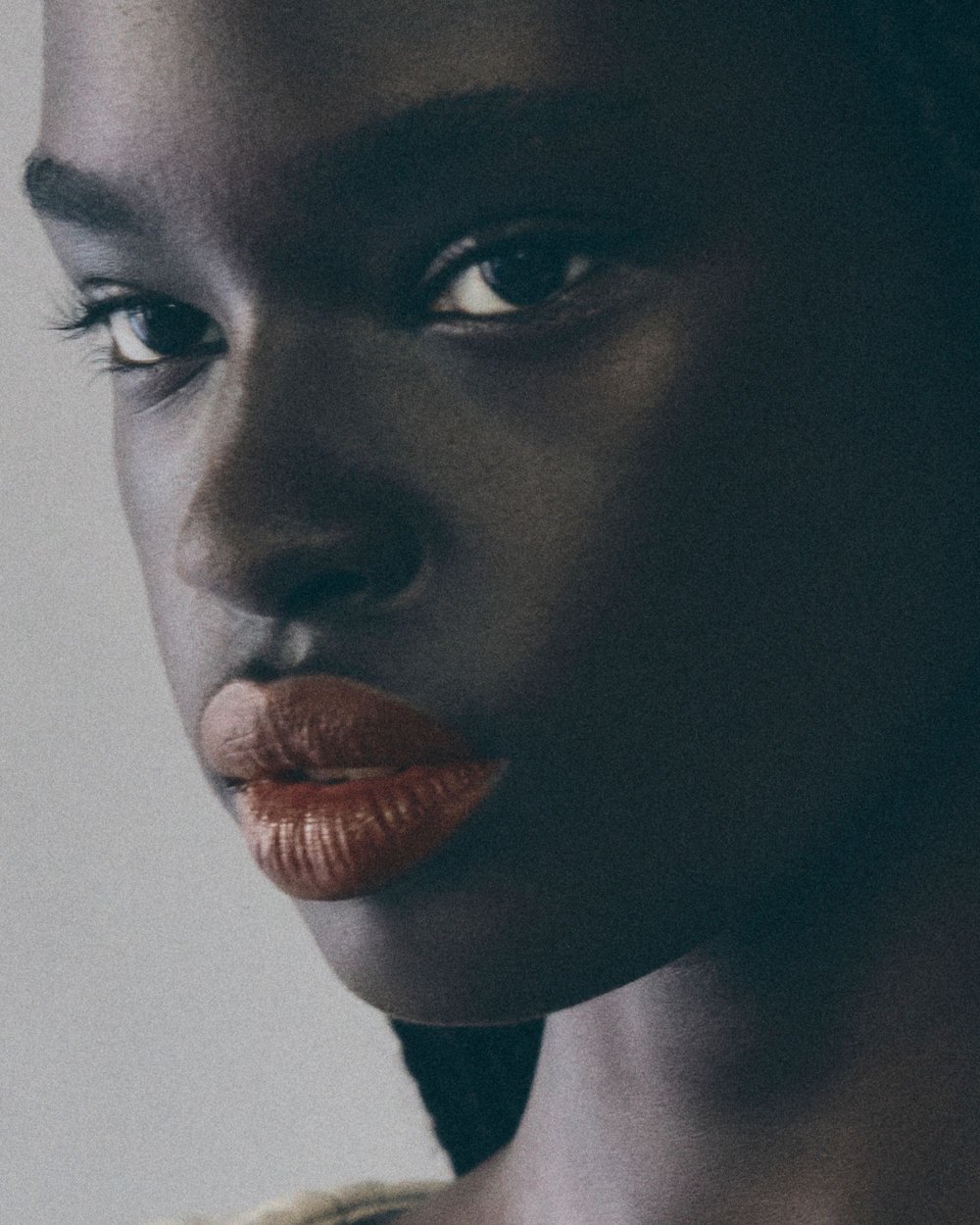 Close-up portrait of a beautiful dark-skinned woman with red lipstick, eyes looking into the camera, against a neutral background.