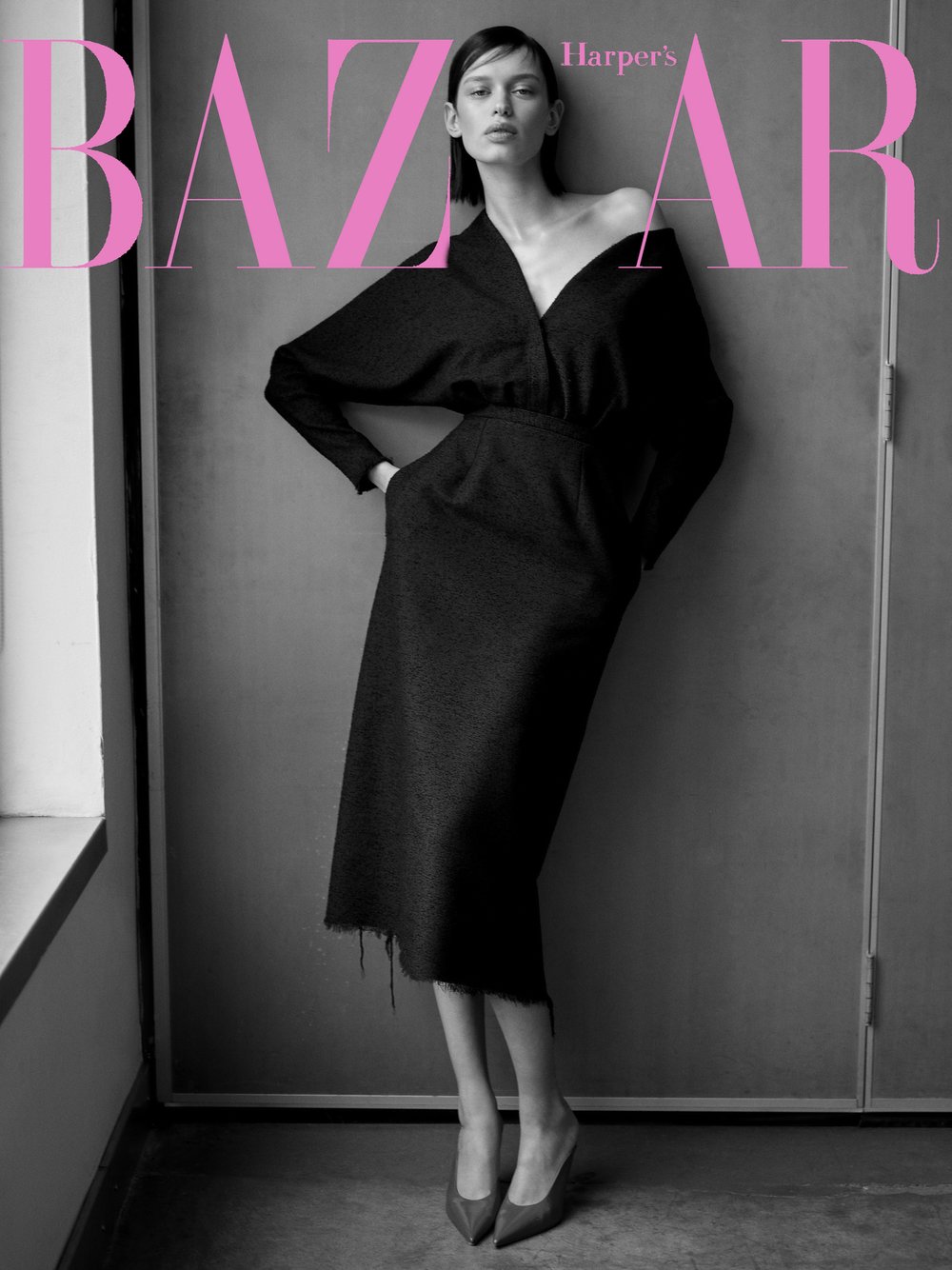 Fashion editorial shot of a slender woman in a dark, draped dress and heels, featured on the cover of Harper's Bazaar magazine.