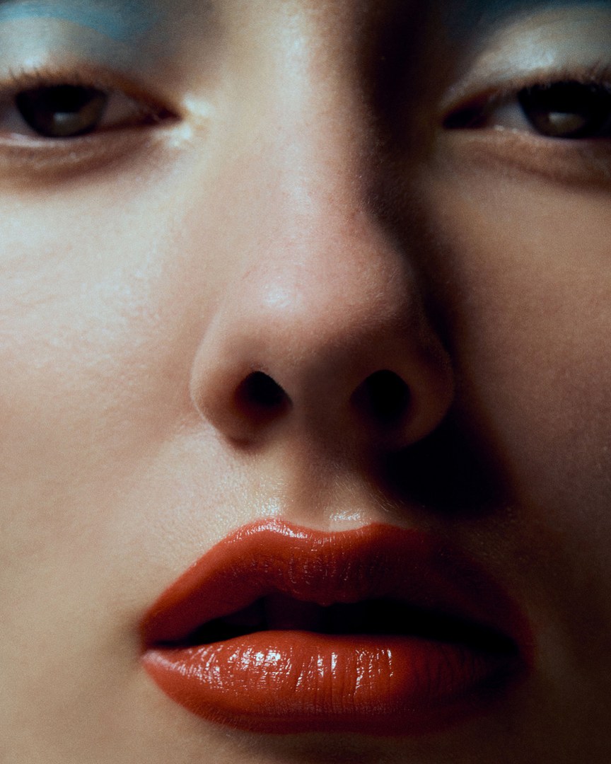 Close-up portrait of a woman with red lipstick and blue eyeshadow; beauty shot with focus on face, makeup, and skin texture.
