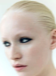 Close up portrait of a blonde model with dramatic dark eyeliner and slicked back hair against a plain white background