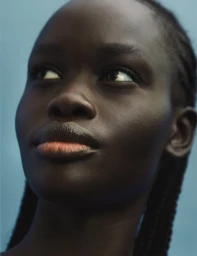 Close-up beauty portrait of a Black woman with braided hair looking upward against a solid blue background