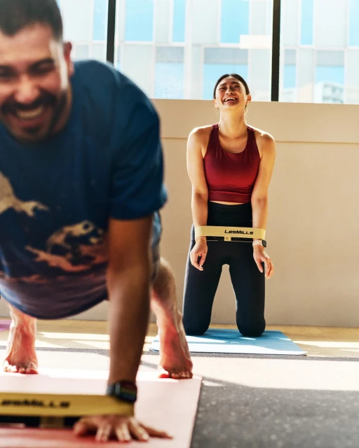 Two people exercising in a studio with resistance bands and yoga mats in a brightly lit indoor space. Fitness and exercise.