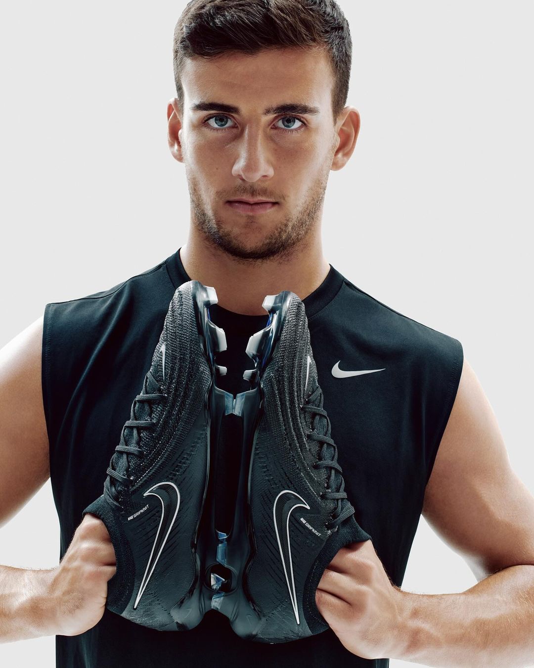 Athletic man holds black Nike soccer shoes against a light backdrop, showcasing modern sportswear and athletic performance.