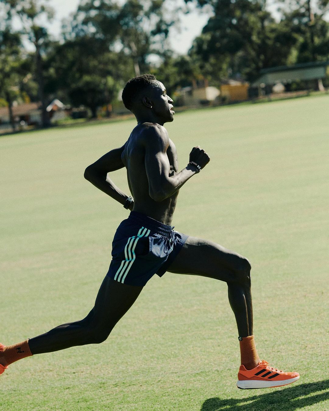 A Black male runner strides across a sunny green field in mid-motion, showcasing fitness and athletic prowess in a natural outdoor setting.
