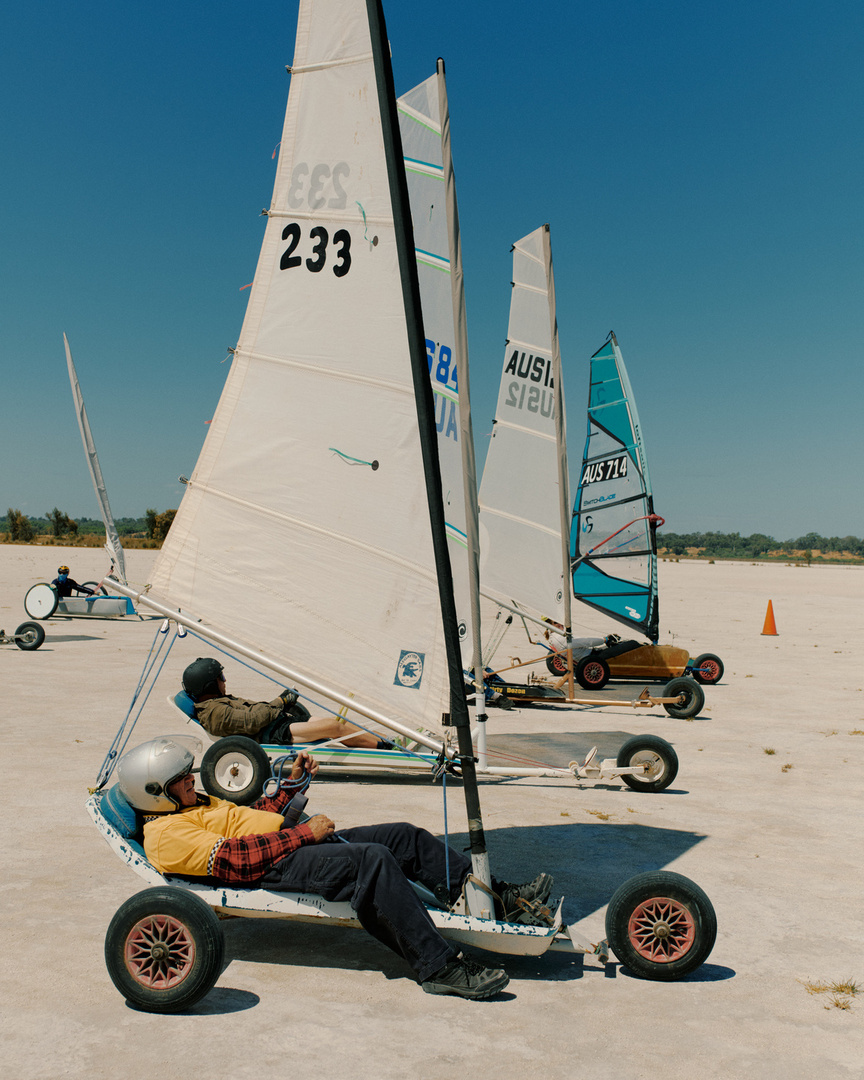 Land sailing vehicles with white sails and drivers on a flat plain under a clear sky on a sunny day. Outdoor land yachting scene.