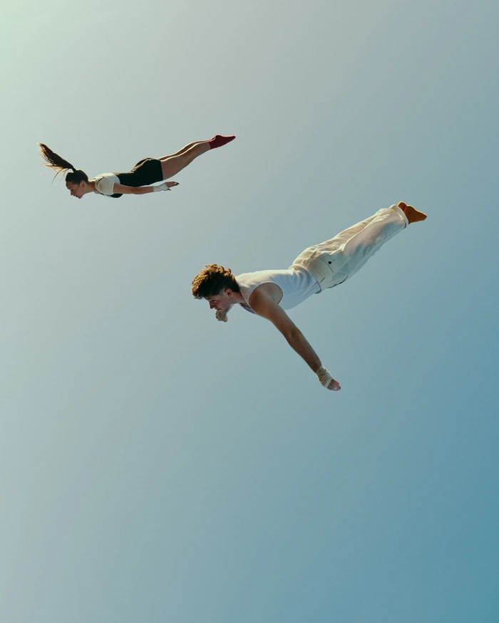 Two acrobats mid-air against a clear blue sky captured by photographer Chris Gurney in Sydney