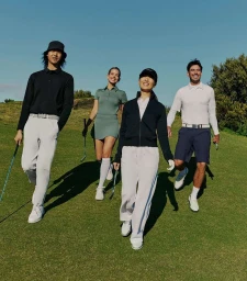 Group of four golfers walking on a grassy course in athletic wear under a clear blue sky