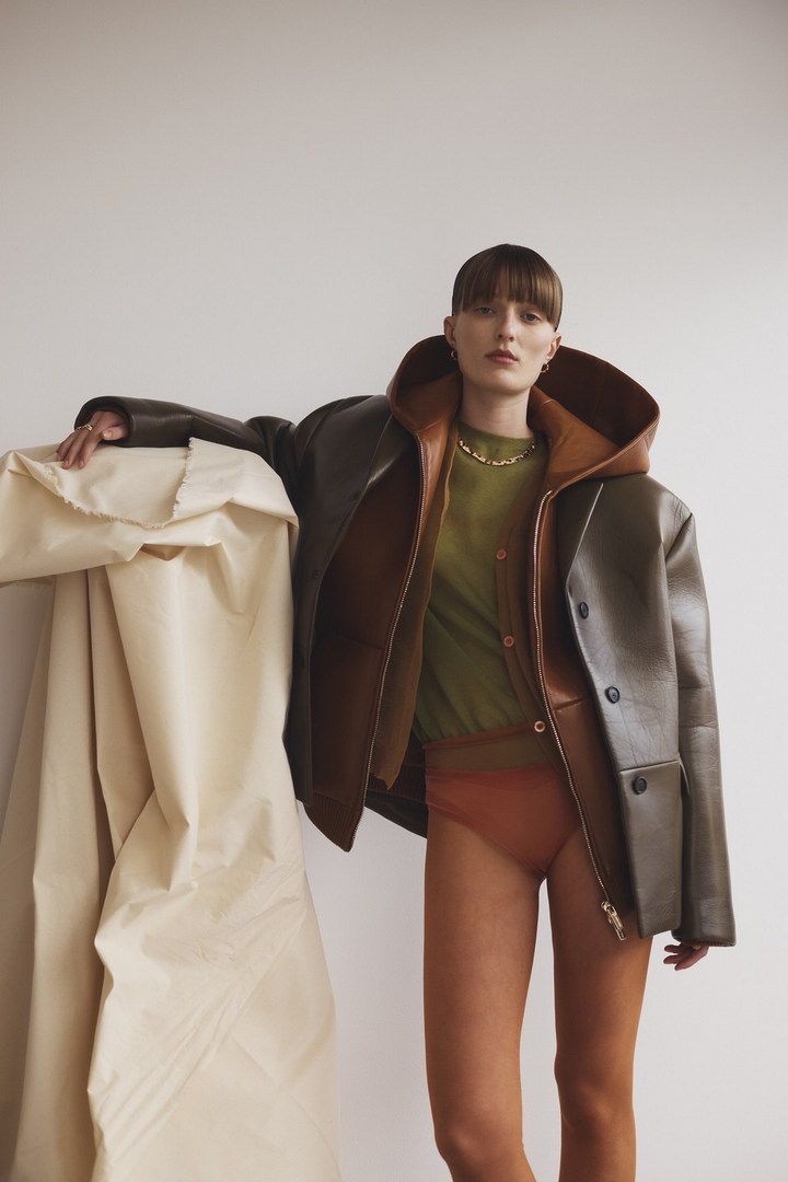 Stylish female model in a reversible brown leather jacket and green top, posing against a cream backdrop with draped fabric.