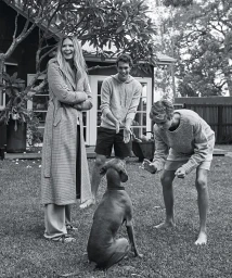 Black and white portrait of a woman, two young men, and a dog on a grassy lawn outside a house styled by Kate Darvill.