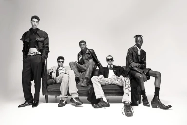 Five models styled by Miguel Urbina Tan posing on and around a dark couch in a studio setting.