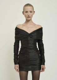 Model in off-the-shoulder black ruched mini dress standing against a plain white background