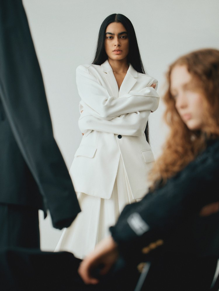 Fashion photo features a confident woman in a white blazer, arms crossed, with two women in black blazers in the foreground.