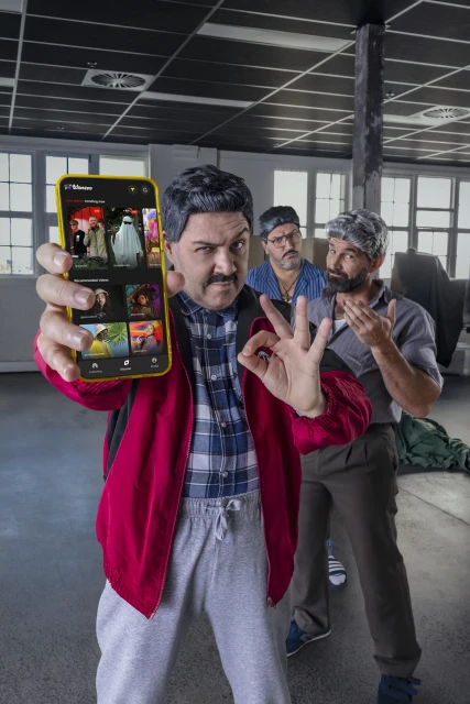Three adult males display a smartphone showing the Visie platform against a background of an open workspace with visible ceiling pipes.