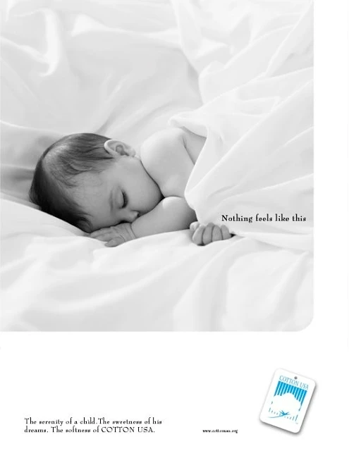 Black and white photograph of an infant sleeping peacefully wrapped in soft white cotton sheets.