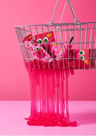 Shopping basket filled with red and pink products with a dripping pink goo on a pink background for a beauty advertisement.