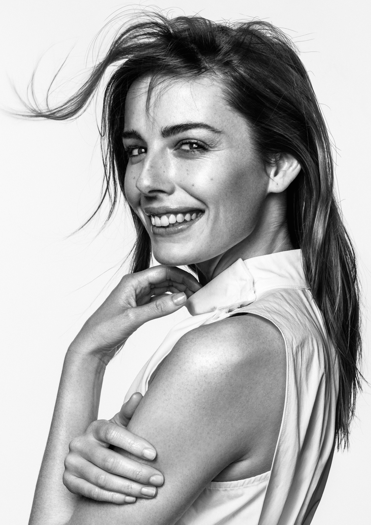 Black and white portrait of a smiling adult woman with long brown hair, wearing a sleeveless top, set against a neutral background.