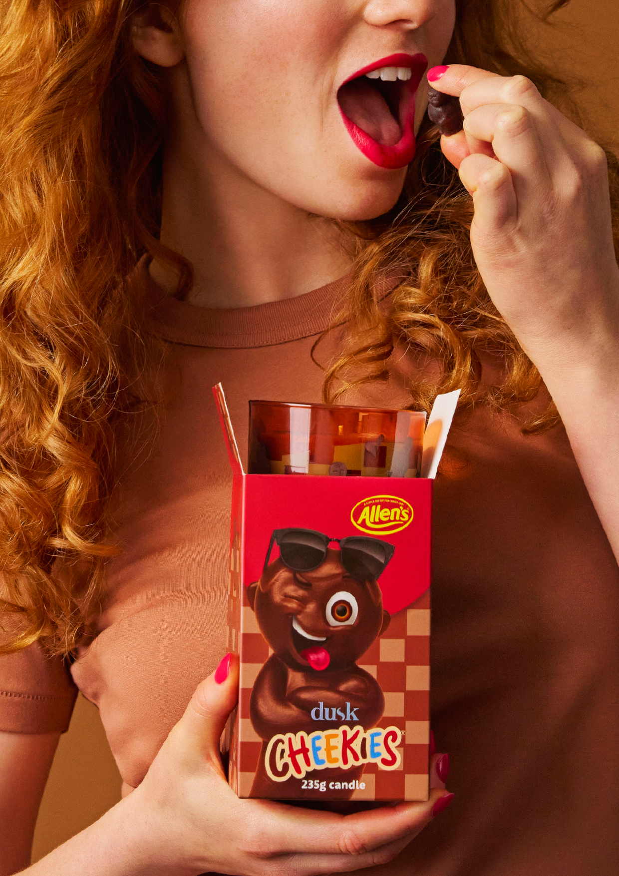 Woman eating dusk CHEEKIES Allen's candy with red lipstick and a red hair against a brown background, close-up shot.