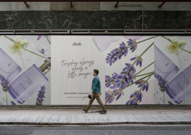 Advertising billboard with a cologne bottle, lavender, and flowers, featuring an adult male in motion on an urban sidewalk.