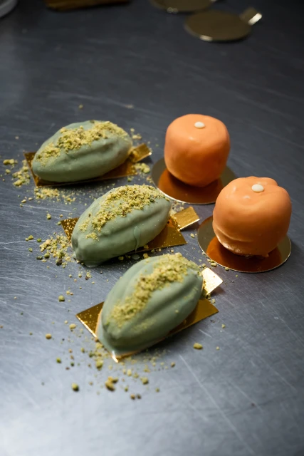 Green and orange petit fours on a gray surface. Food photography showcasing small, colourful pastries decorated with pistachio crumbs.