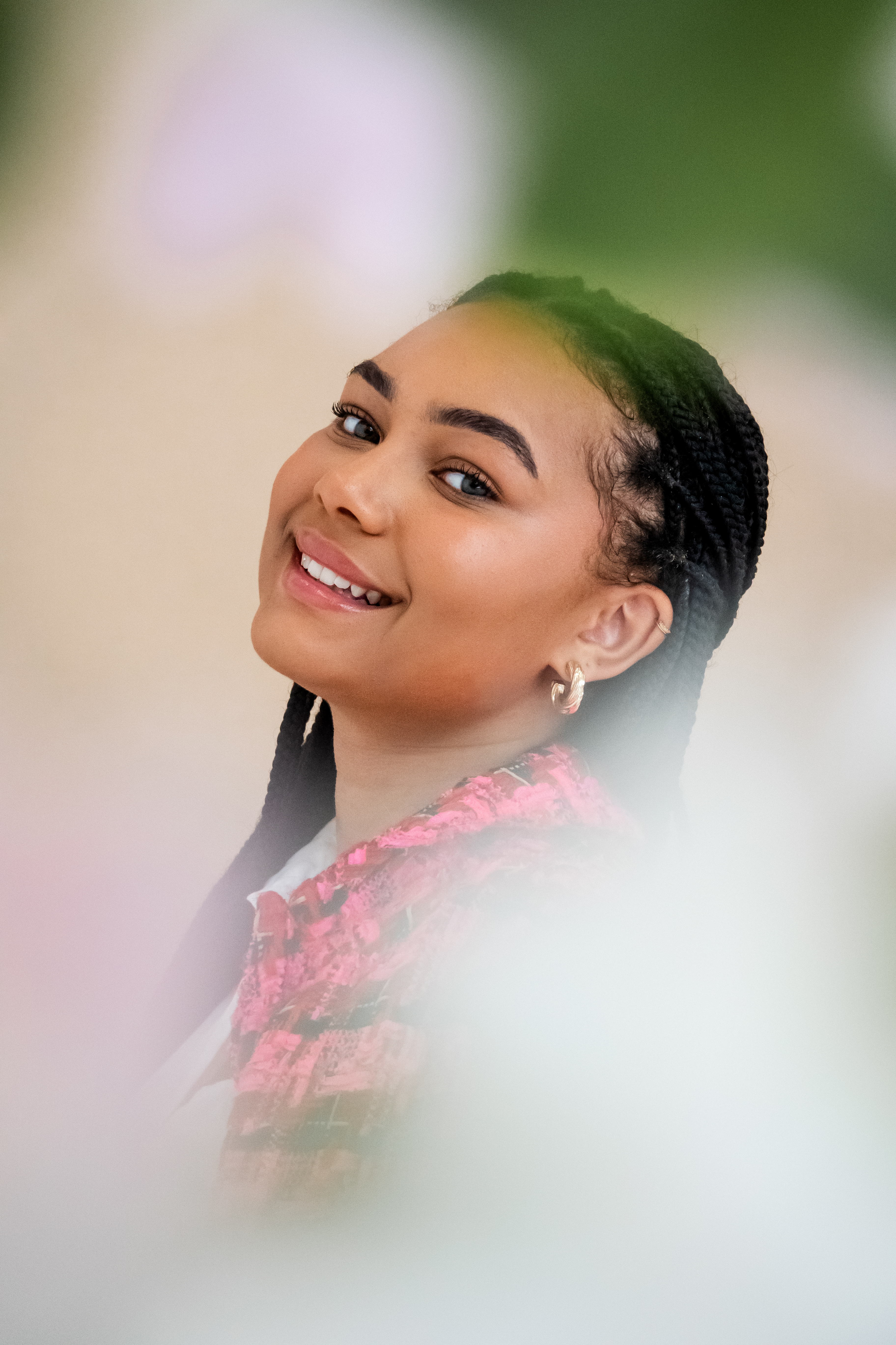 Portrait of smiling young woman with braided hair wearing a pink patterned jacket and small hoop earrings